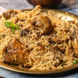 Close-up of aromatic chicken biryani served on a brass plate with garnishes, showcasing Indian culinary art.
