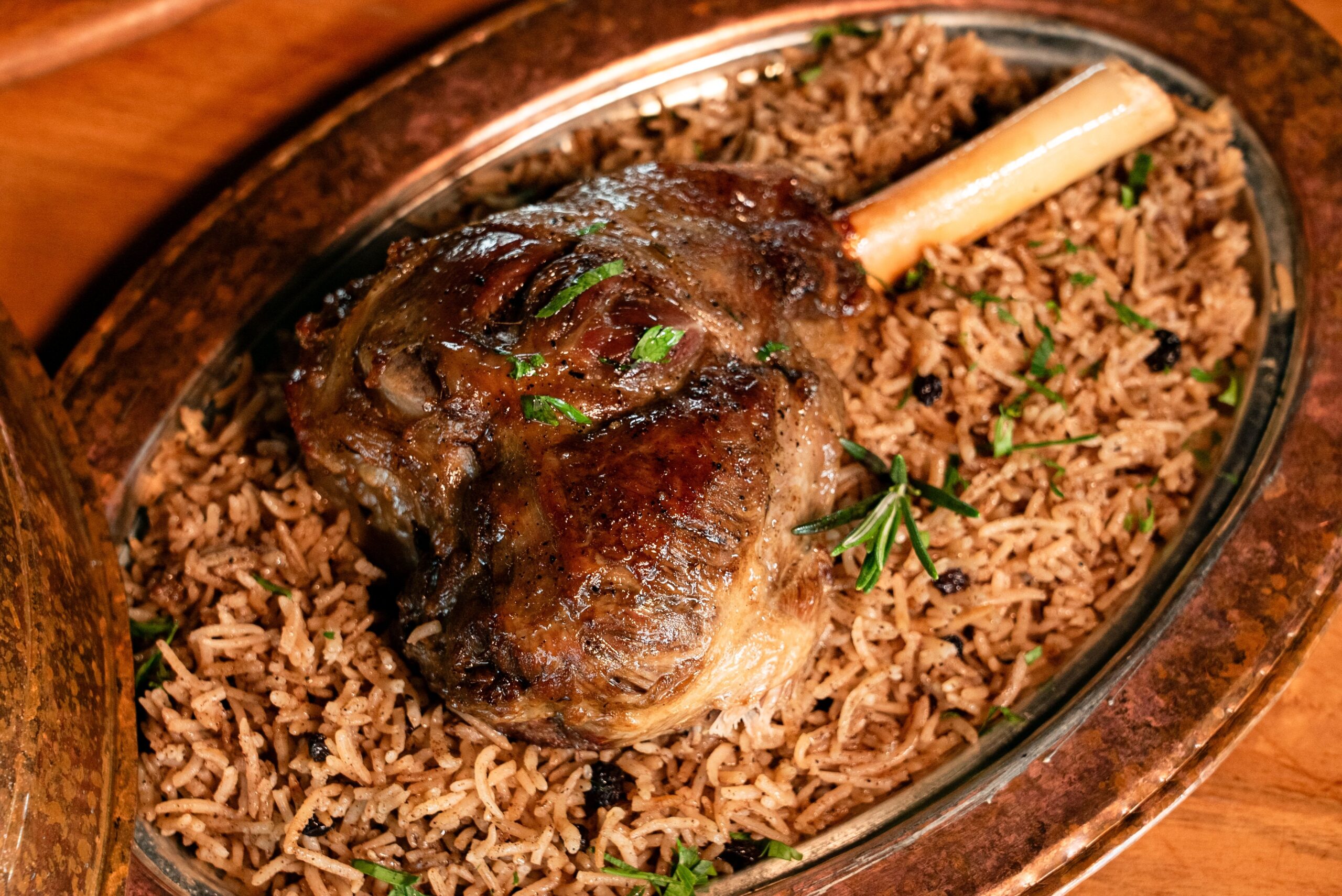Juicy roasted lamb shank served on aromatic basmati rice garnished with herbs.